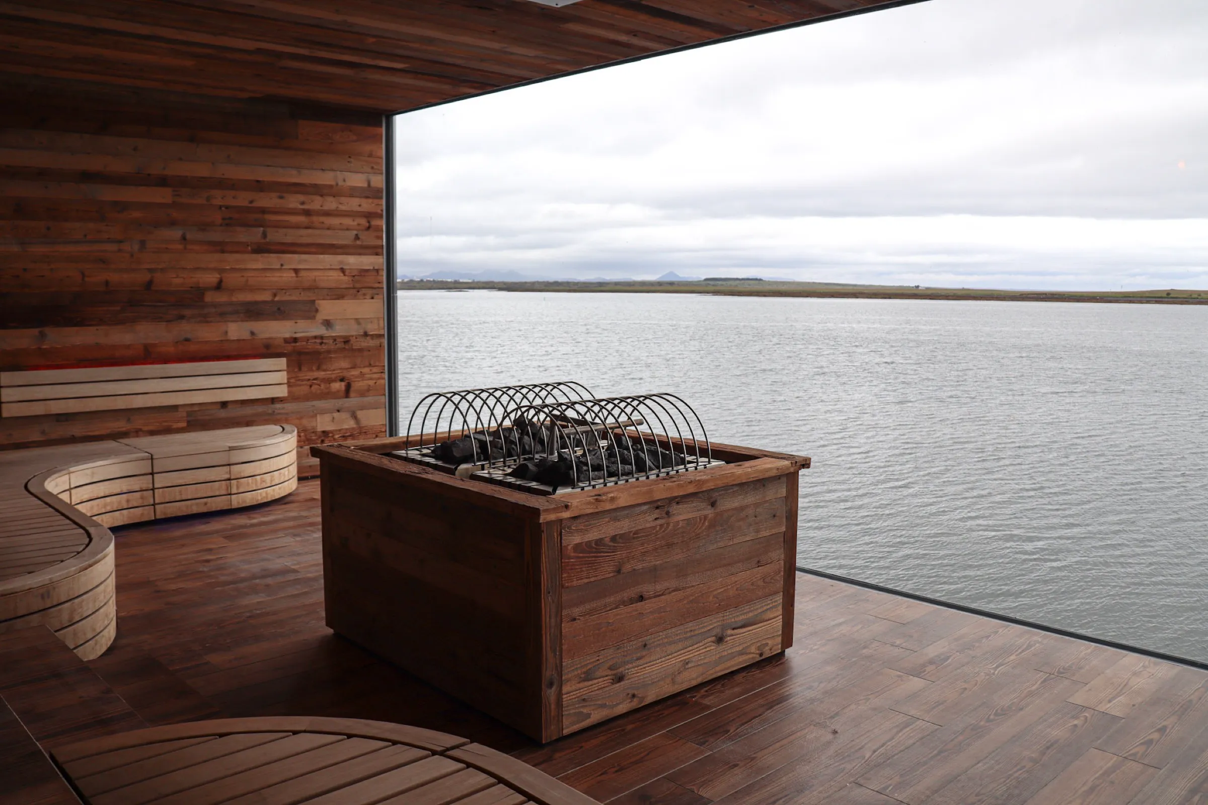 Sauna con calefactor eléctrico en una caja de madera y un ventanal hacia el mar