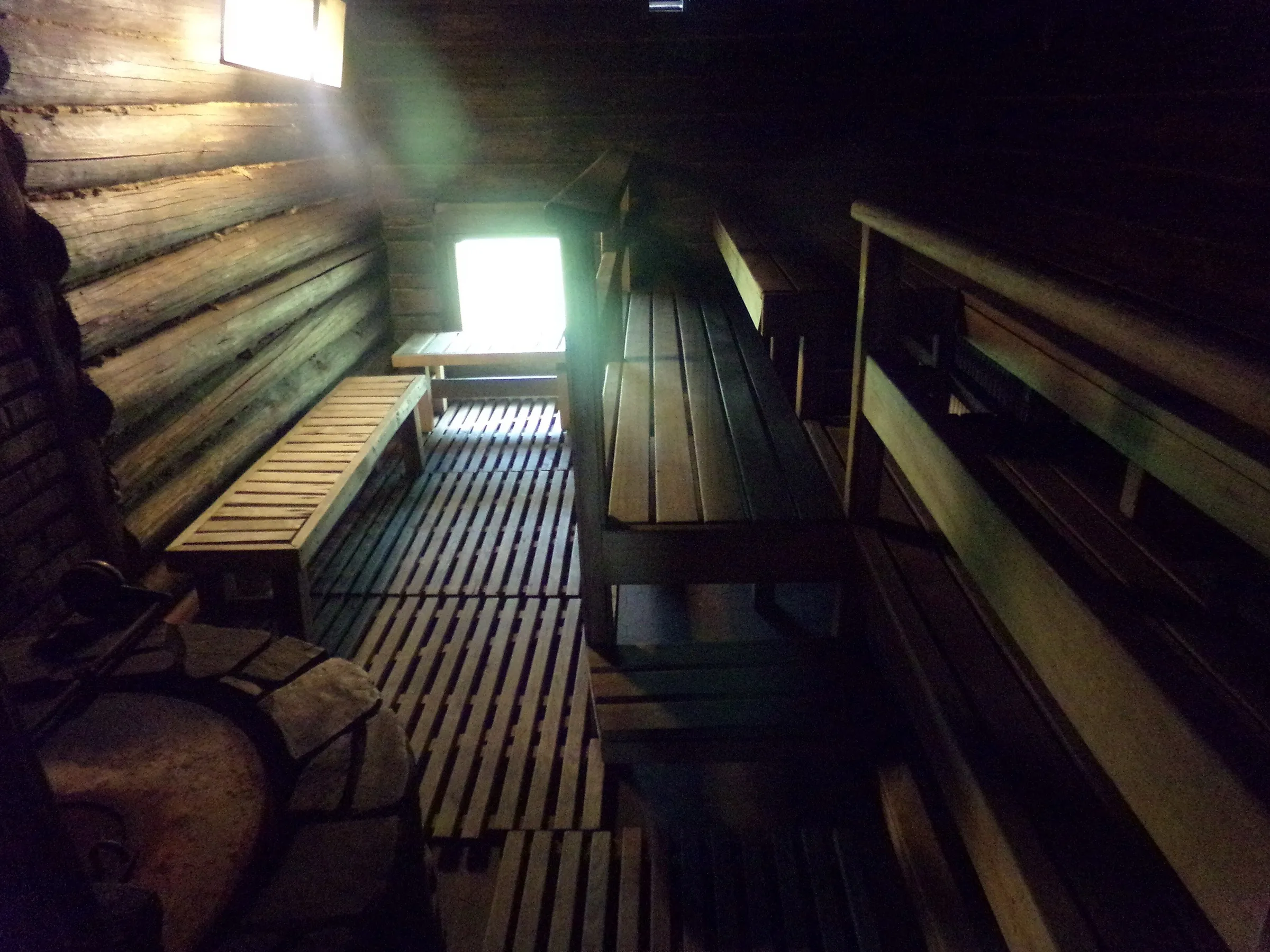 Interior de una sauna de troncos en penumbra, con luz entrando por la ventana