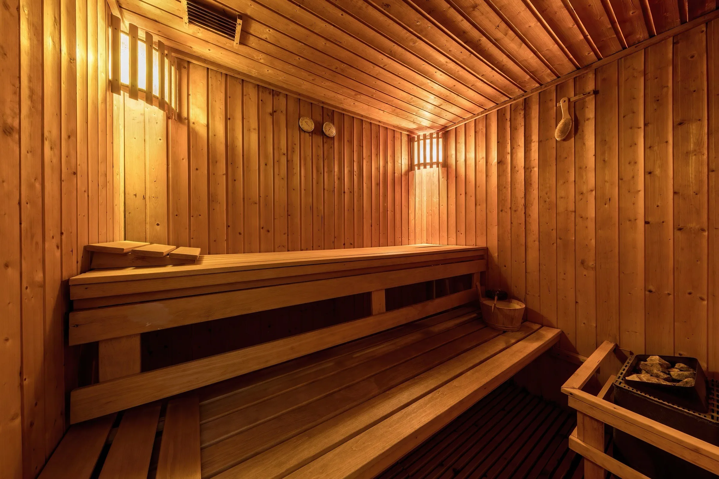 Sauna de madera clara con bancos en dos niveles y luz cálida