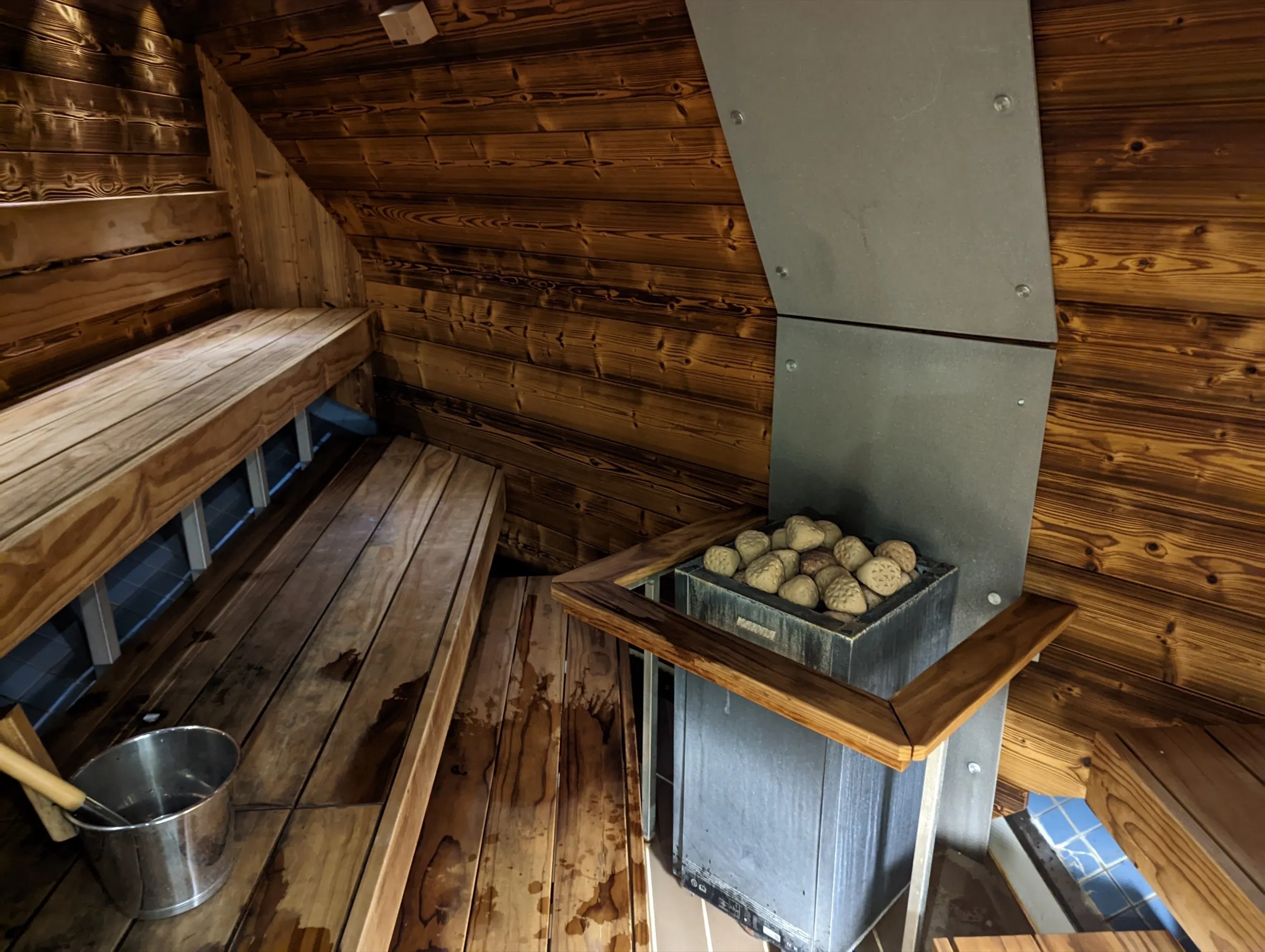 Sauna revestida en madera con estufa y bancos en ángulo