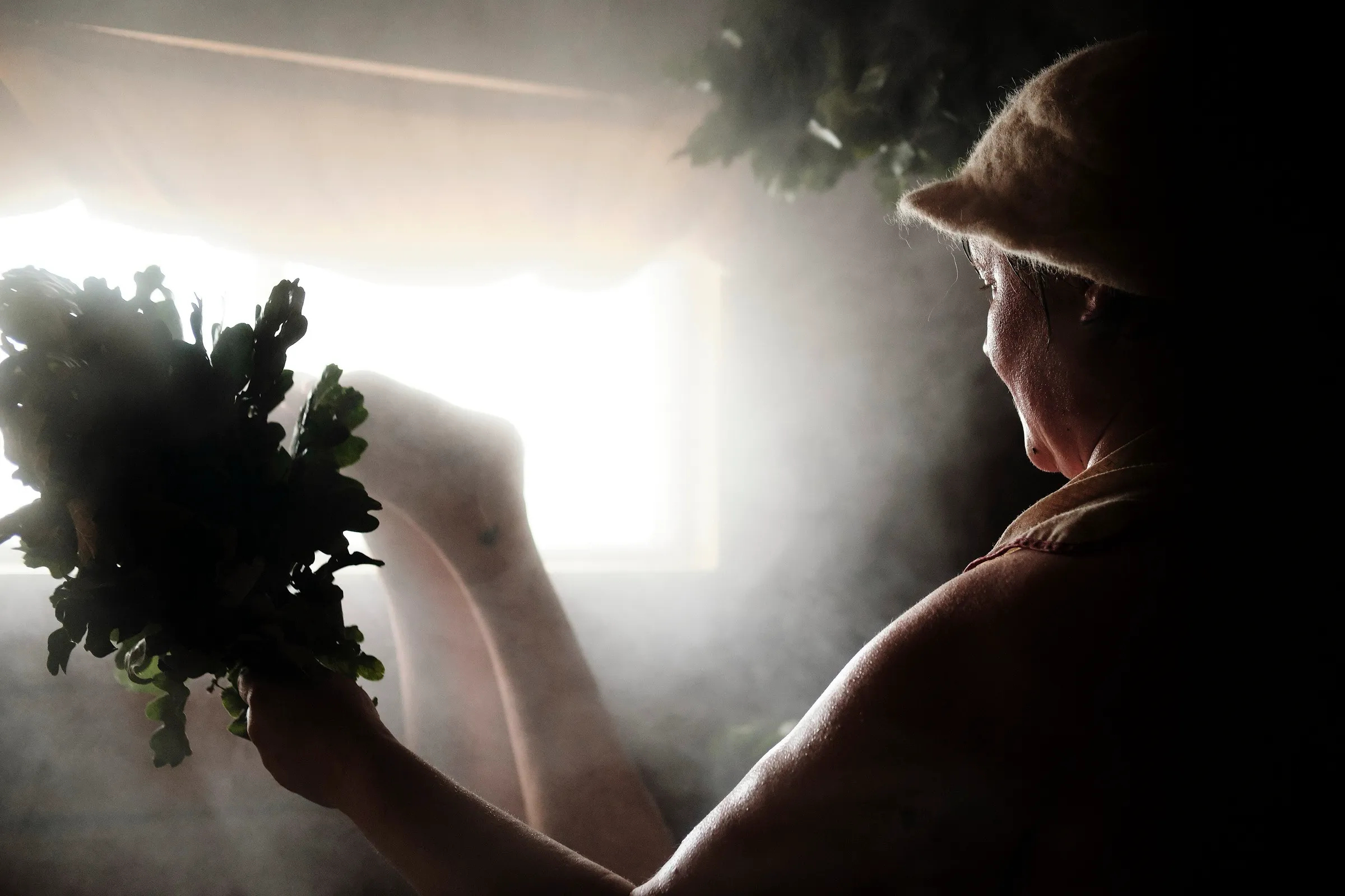 Vapor iluminado por la ventana de una sauna, con un ramillete de abedul